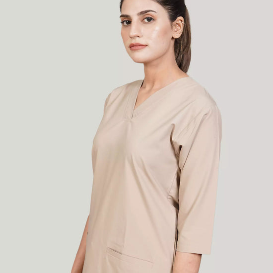 A woman wearing a green scrub set with a V-neckline and 3-quarter sleeves, featuring two bone pockets on the shirt and two pockets on the trousers. She is smiling and standing against a white background.