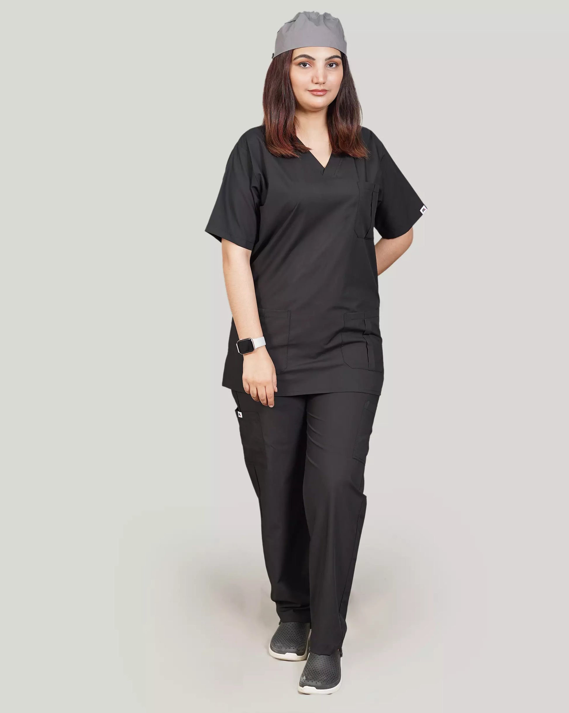 Full-body front view of a female medical professional in a stylish black Medfit unisex scrub set, complete with a matching scrub cap, ideal for modern healthcare uniforms.