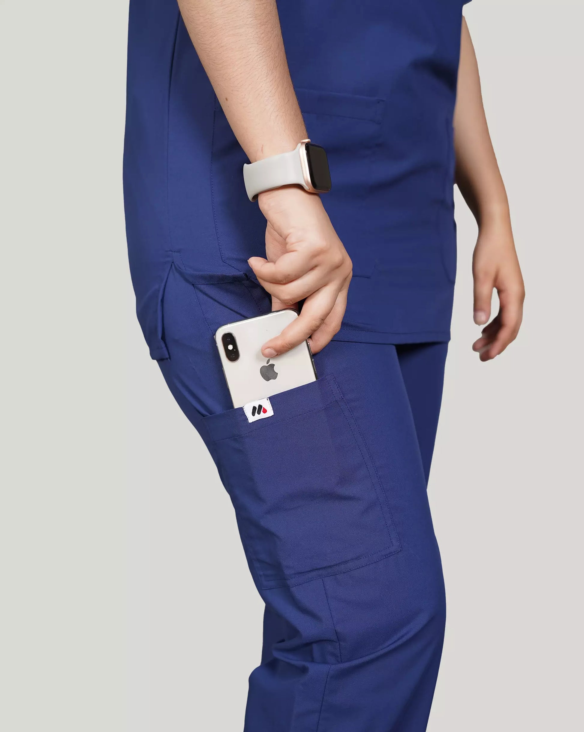 Close-up of a hand inserting a smartphone into the pocket of navy blue Medfit unisex scrub pants, featuring a subtle Medfit logo for practical and professional use.