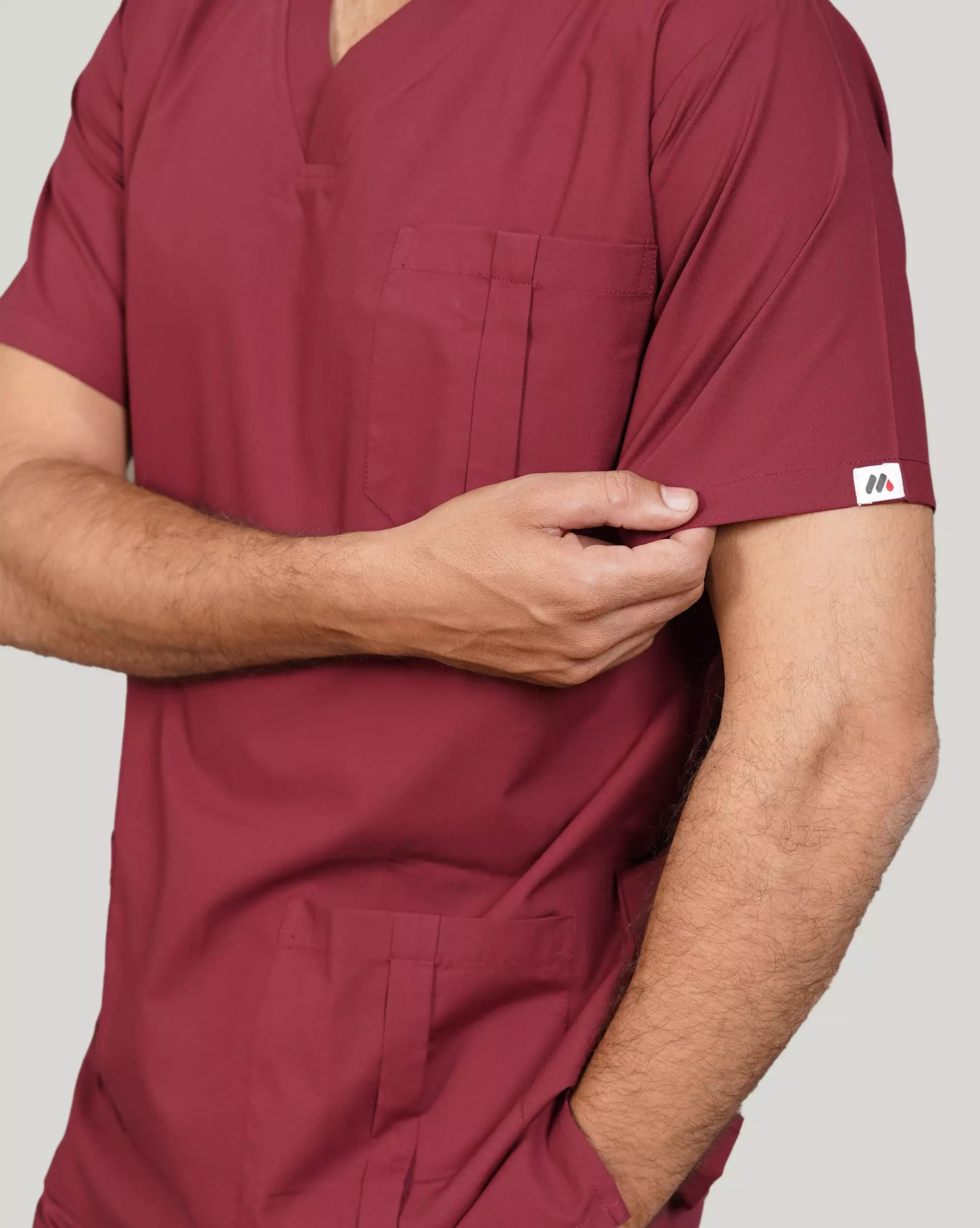 Close-up of a hand inserting a smartphone into the pocket of burgundy Medfit men's scrub top, highlighting functional design and the Medfit logo on the sleeve.