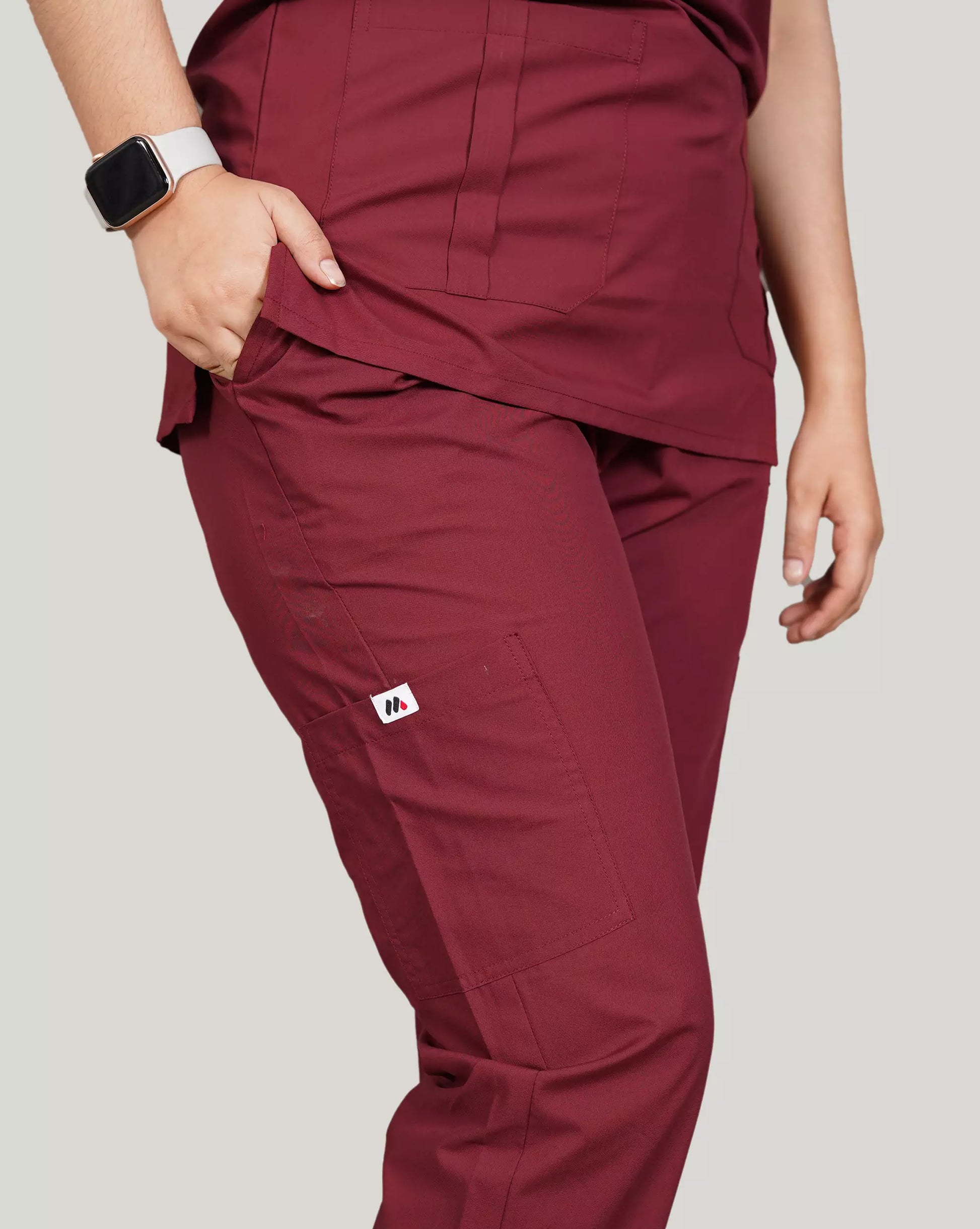 Close-up of a hand inserting a smartphone into the pocket of burgundy Medfit men's scrub top, highlighting functional design and the Medfit logo on the sleeve.