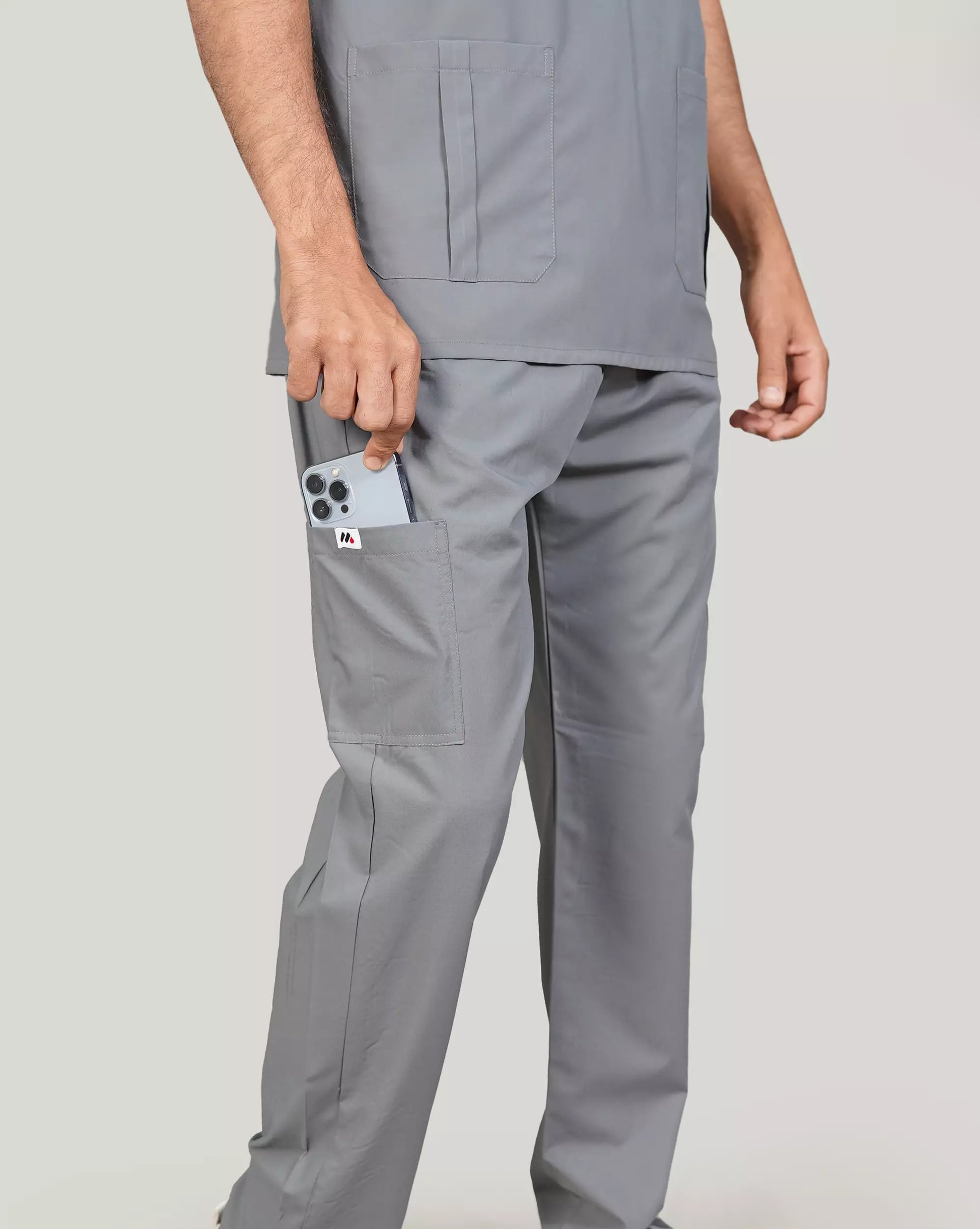 Close-up of a hand inserting a smartphone into the pocket of basic grey Medfit men's scrub pants, emphasizing practical storage and a sleek design for medical professionals.