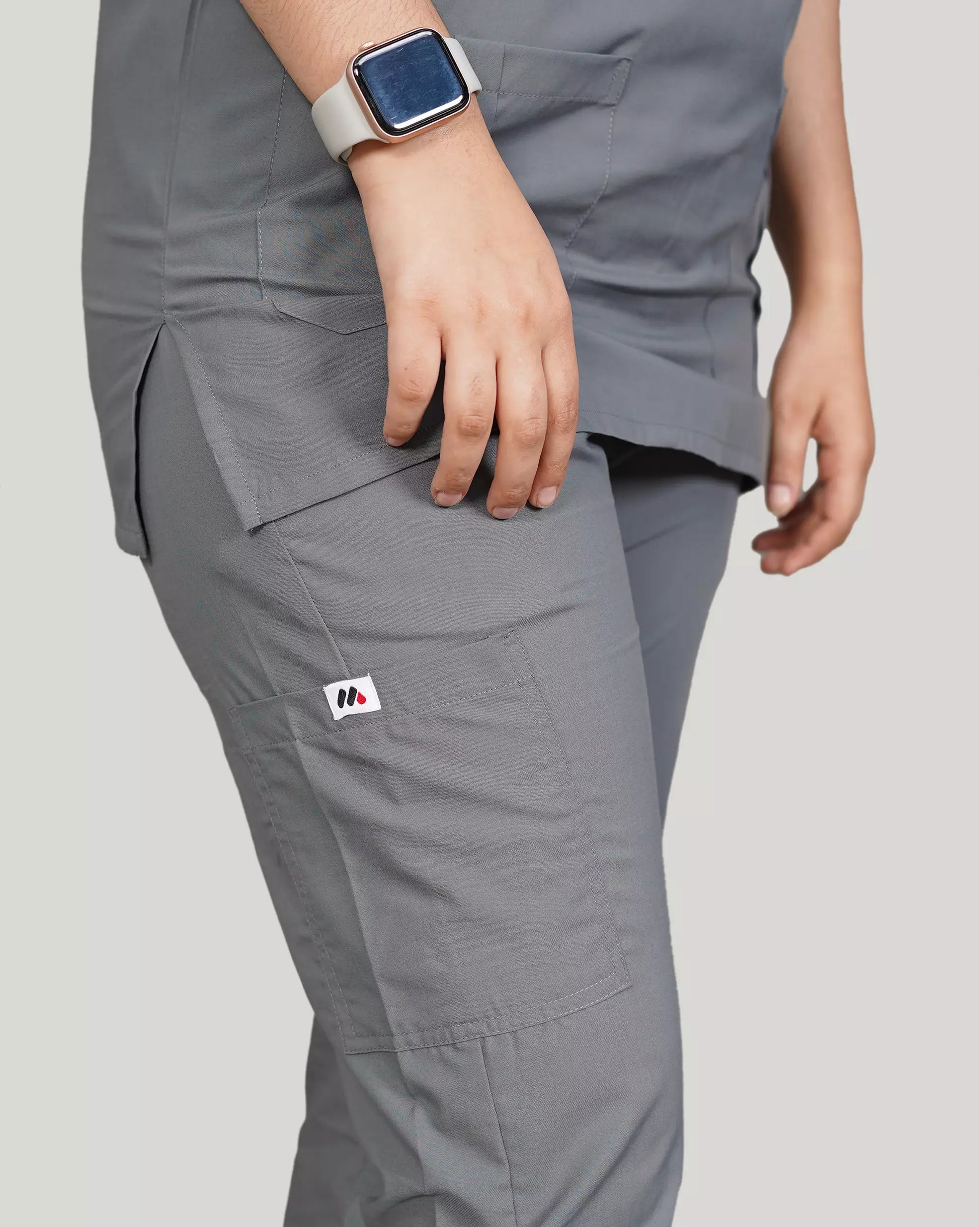 Close-up of a hand resting on a functional pocket of basic grey Medfit unisex scrub pants, featuring the Medfit logo and smartwatch, perfect for busy healthcare professionals.