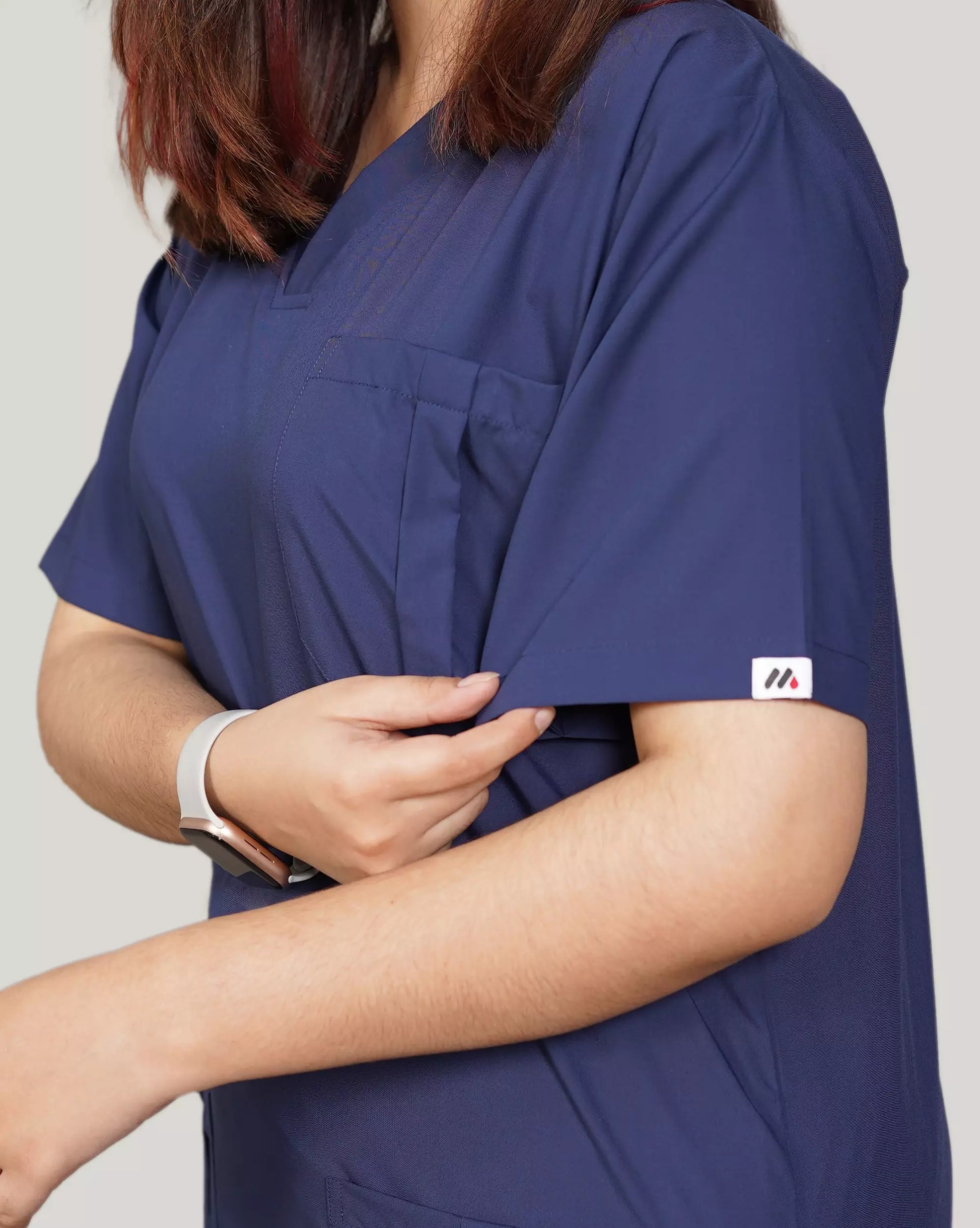 Close-up of a hand adjusting the sleeve of a navy blue Medfit unisex scrub top, highlighting the comfortable fabric and Medfit logo, suitable for medical and healthcare professionals.