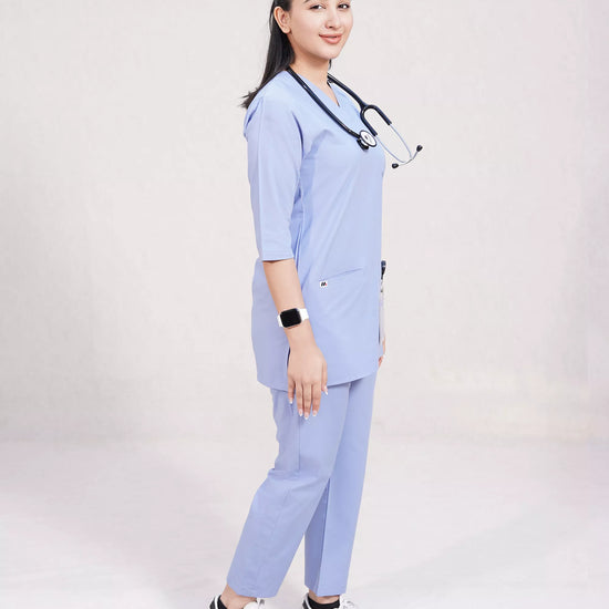 Person wearing a light blue medical scrub set with a stethoscope, on a plain background.