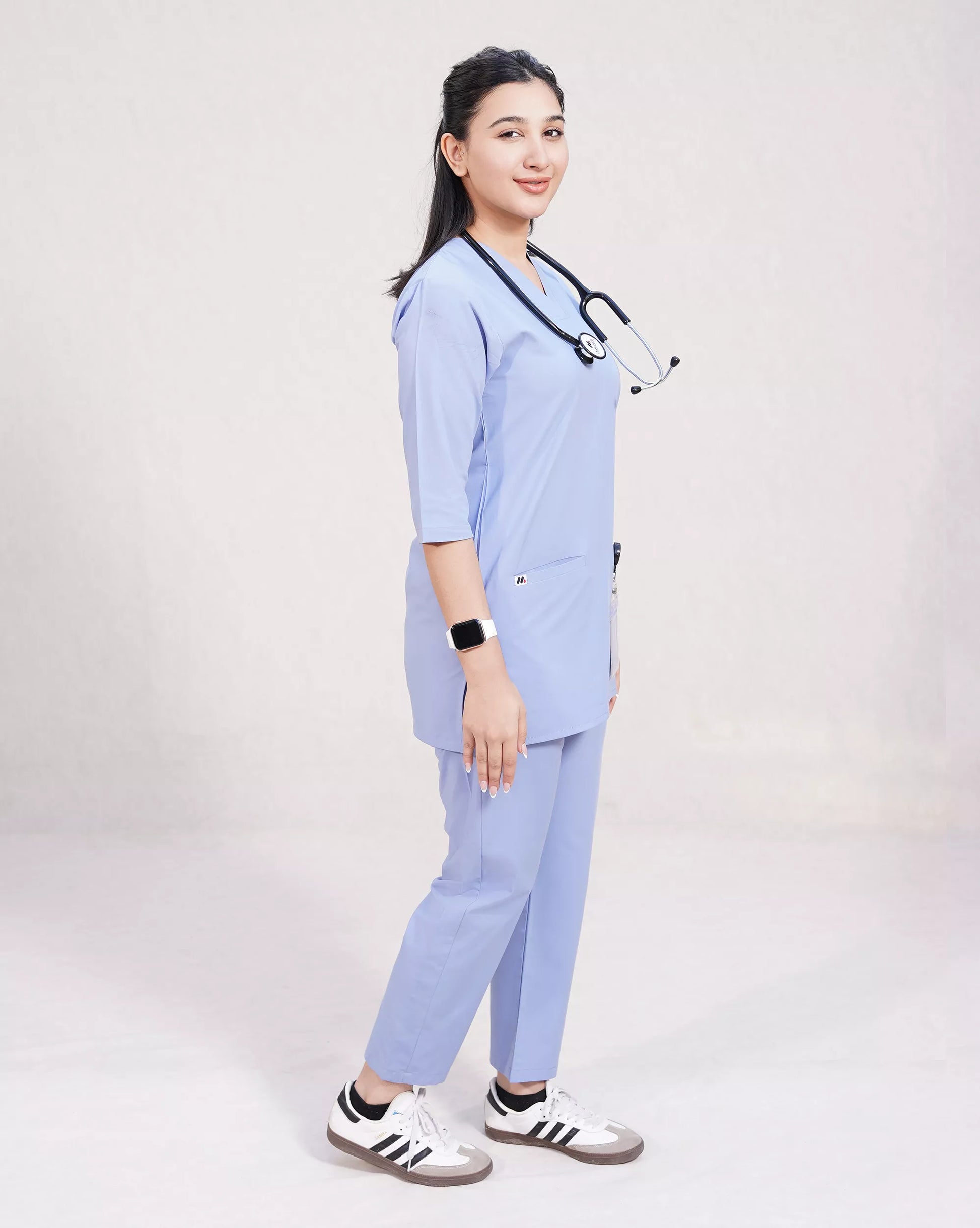 Person wearing a light blue medical scrub set with a stethoscope, on a plain background.
