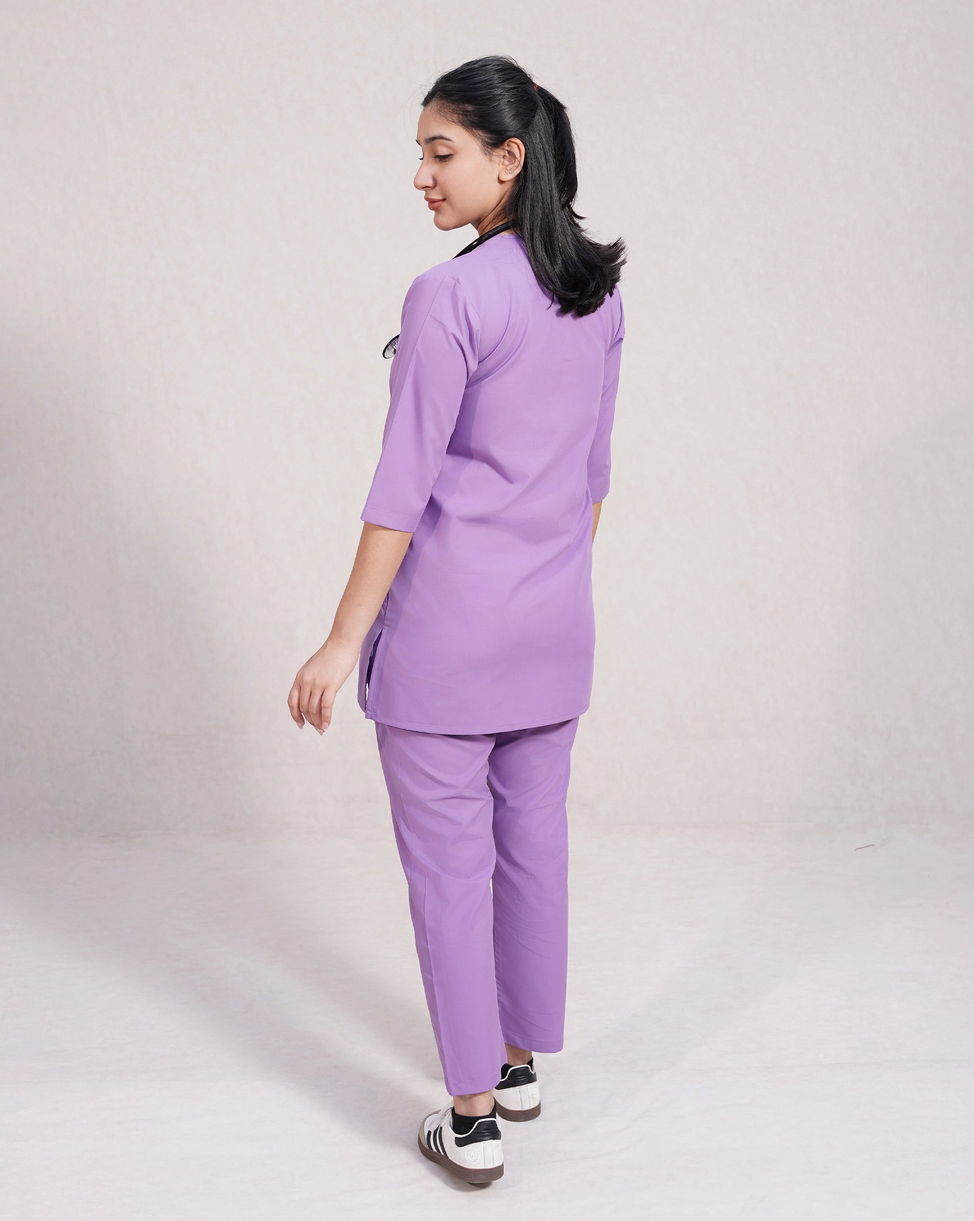 Person wearing a purple scrub set on a plain background