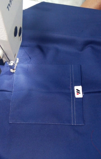 A Custom Men Scrub in Pakistan, top in blue color, showing the front pocket area with stitching details, on a sewing machine.