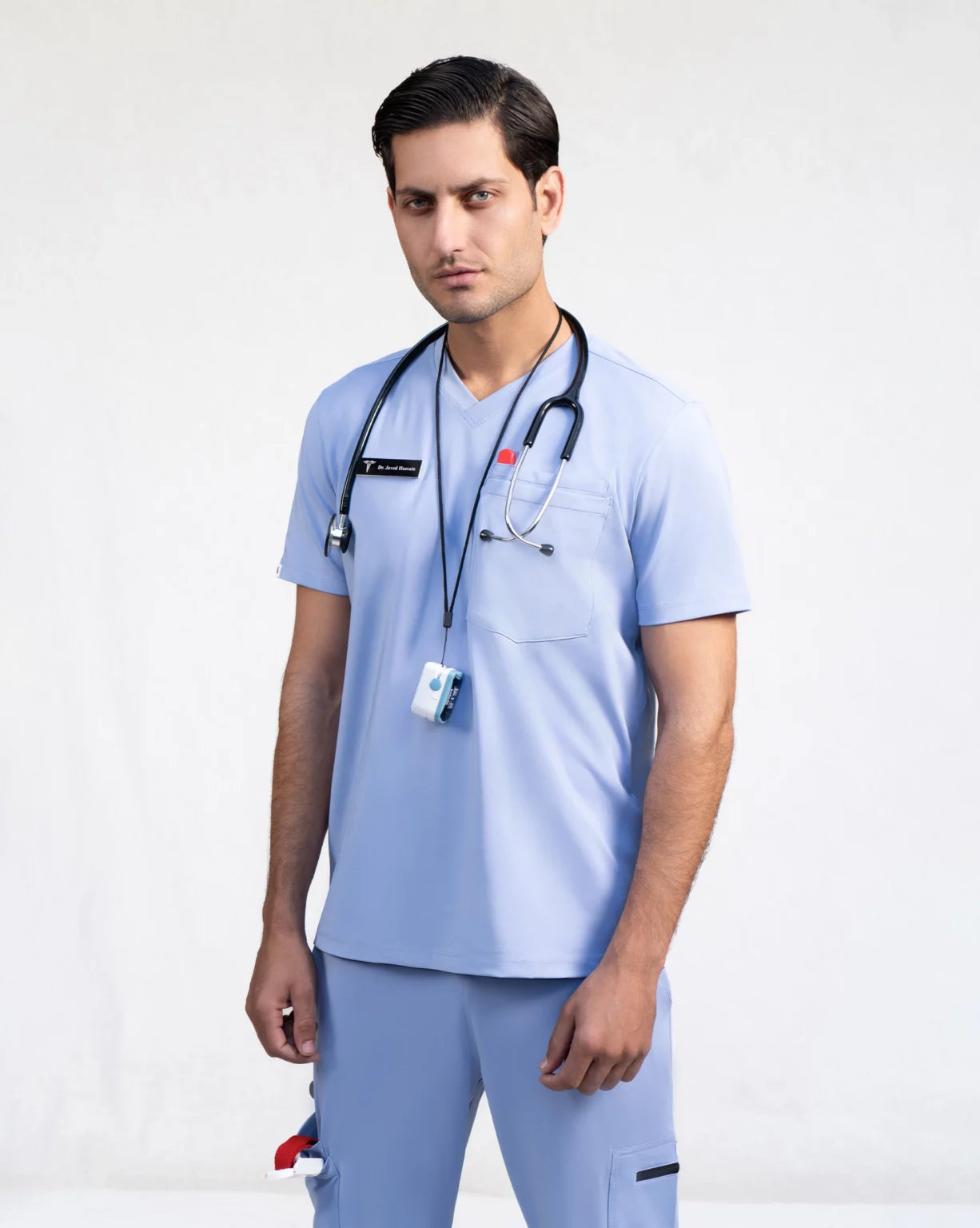 Person wearing a blue medical scrub set with a stethoscope and ID badge on a plain background.