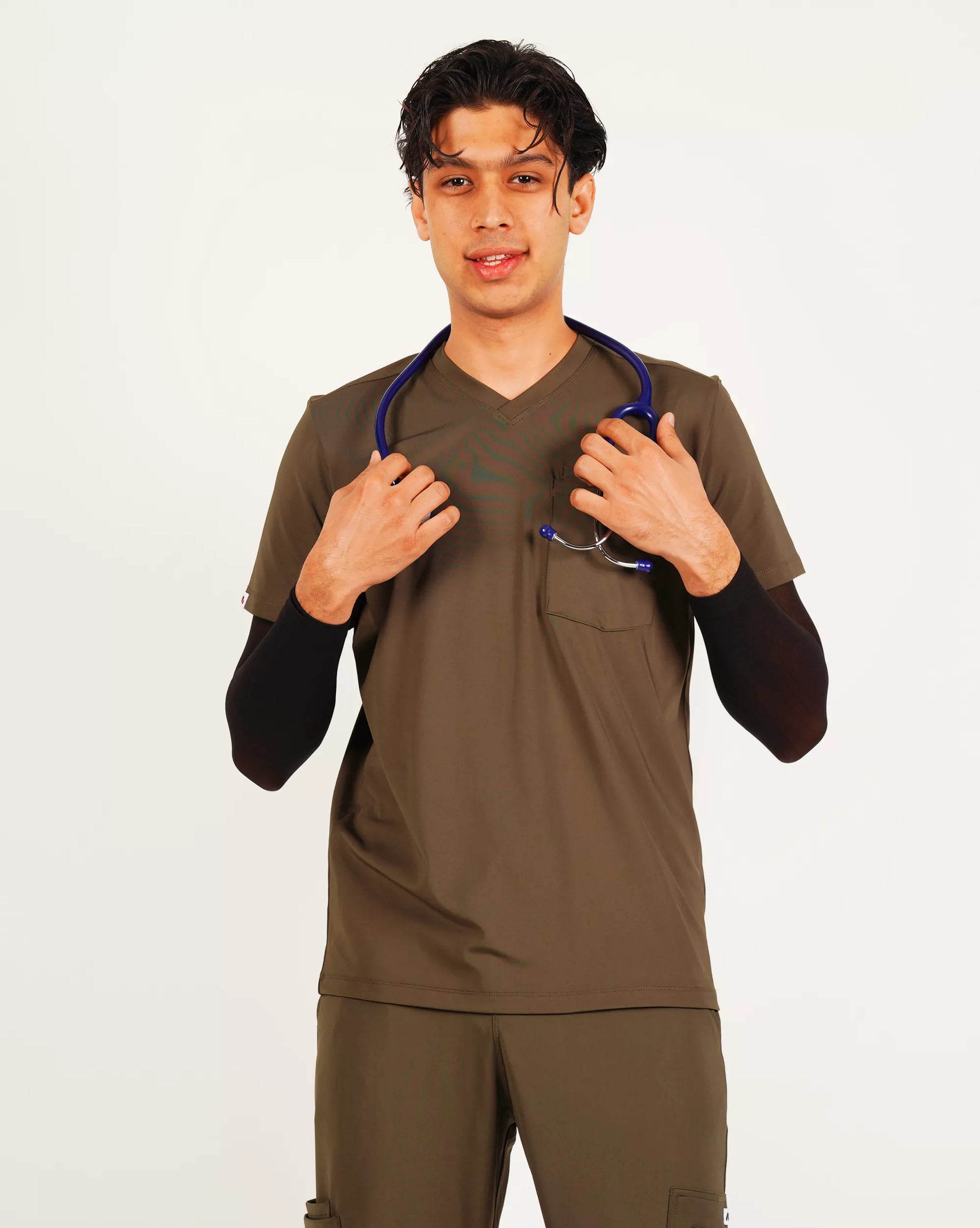A person wearing a green V-neck scrub shirt with a stethoscope around their neck, featuring multiple pockets.