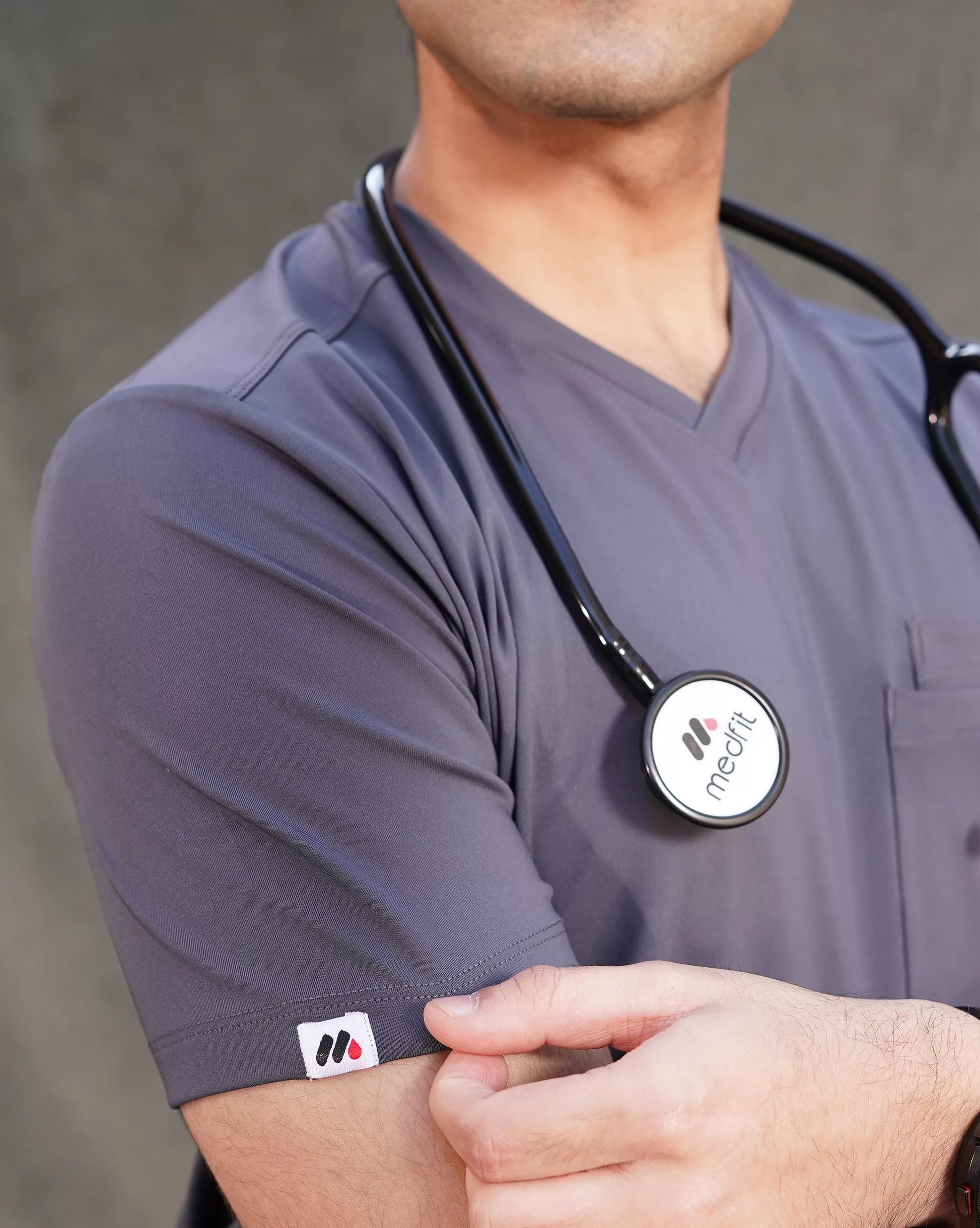 A person wearing a green V-neck scrub shirt with a stethoscope around their neck, featuring multiple pockets.