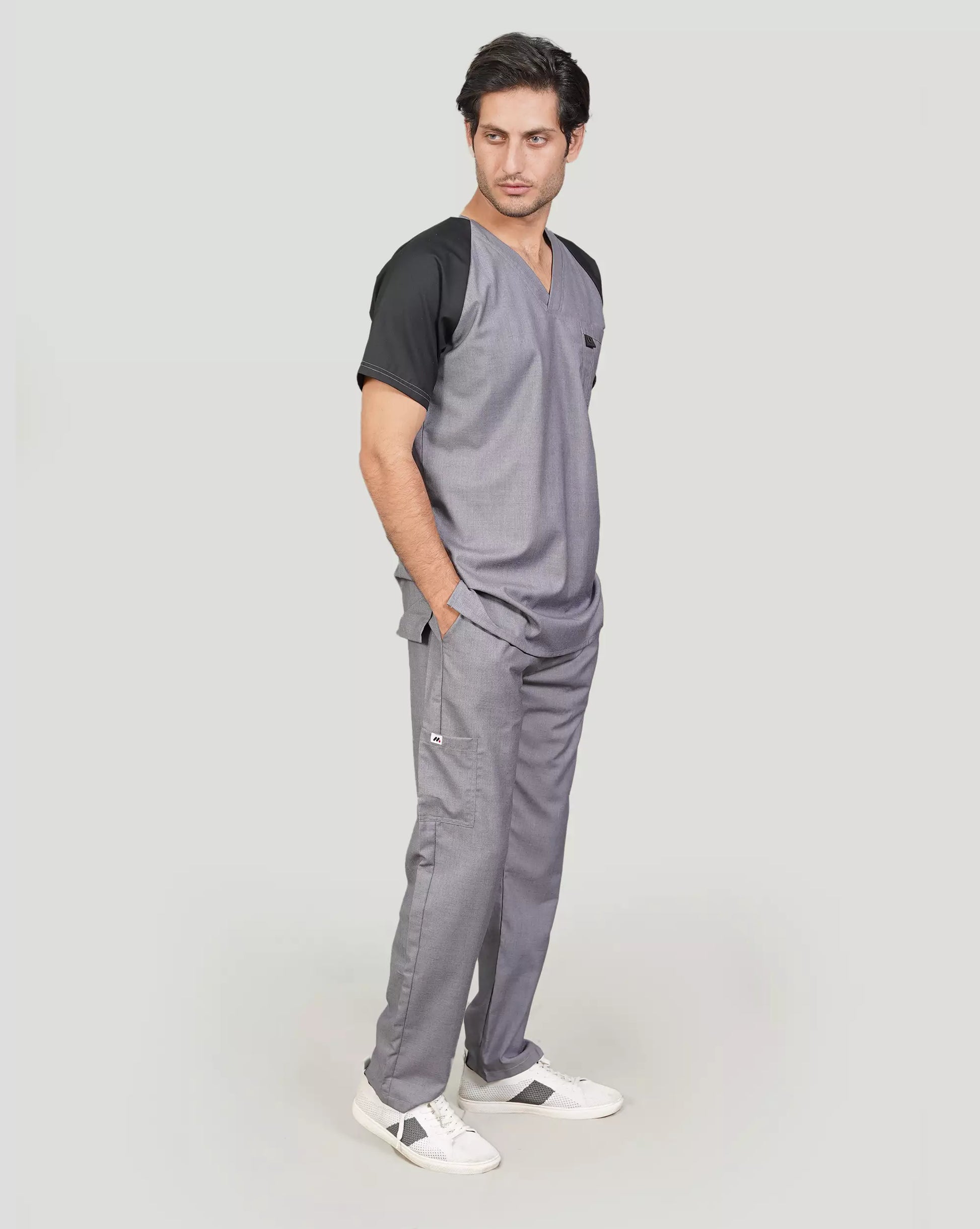 Man wearing gray medical scrubs with a black top on a plain background.