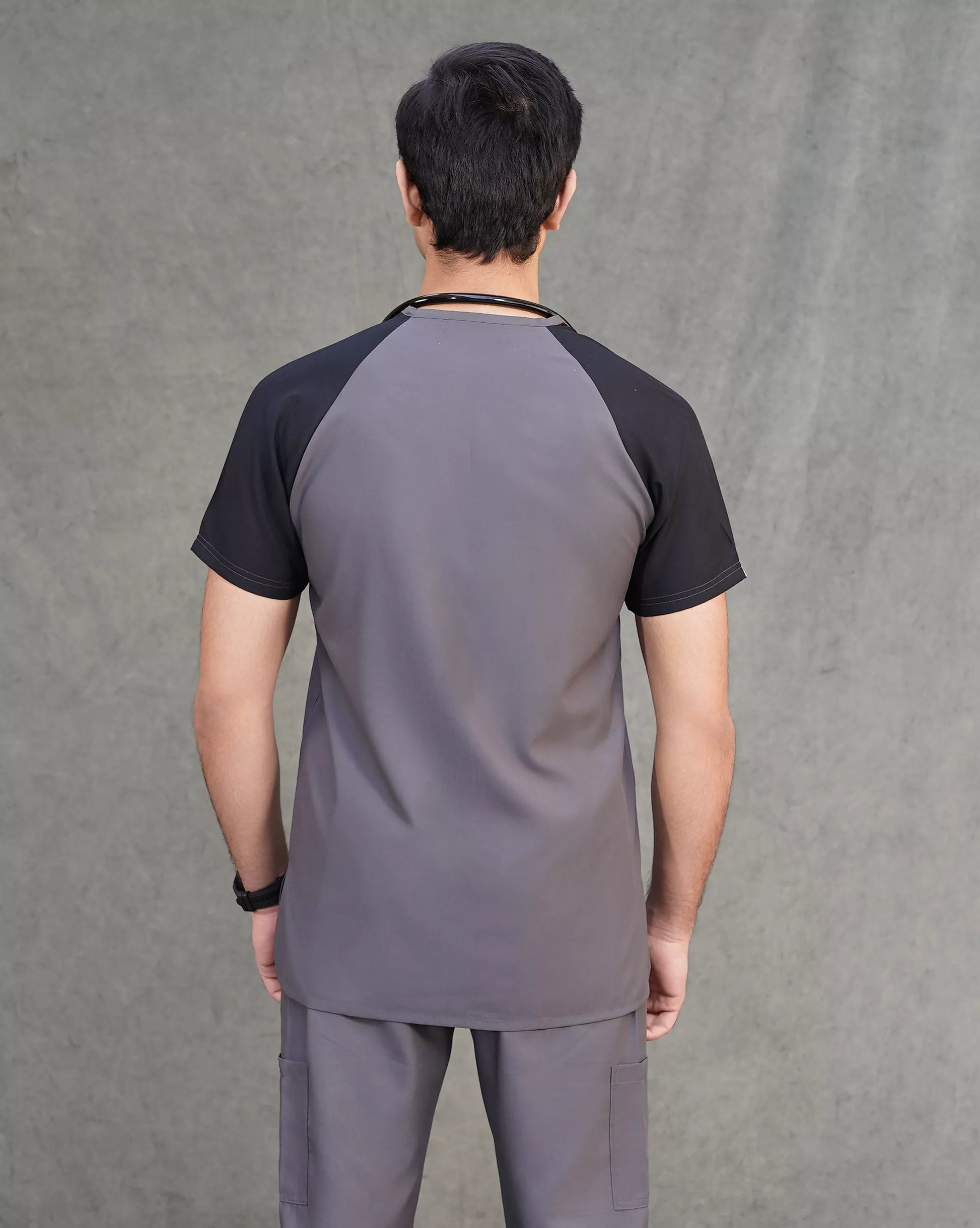 Person wearing a gray and black Premium doctor scrubs top against a gray background.