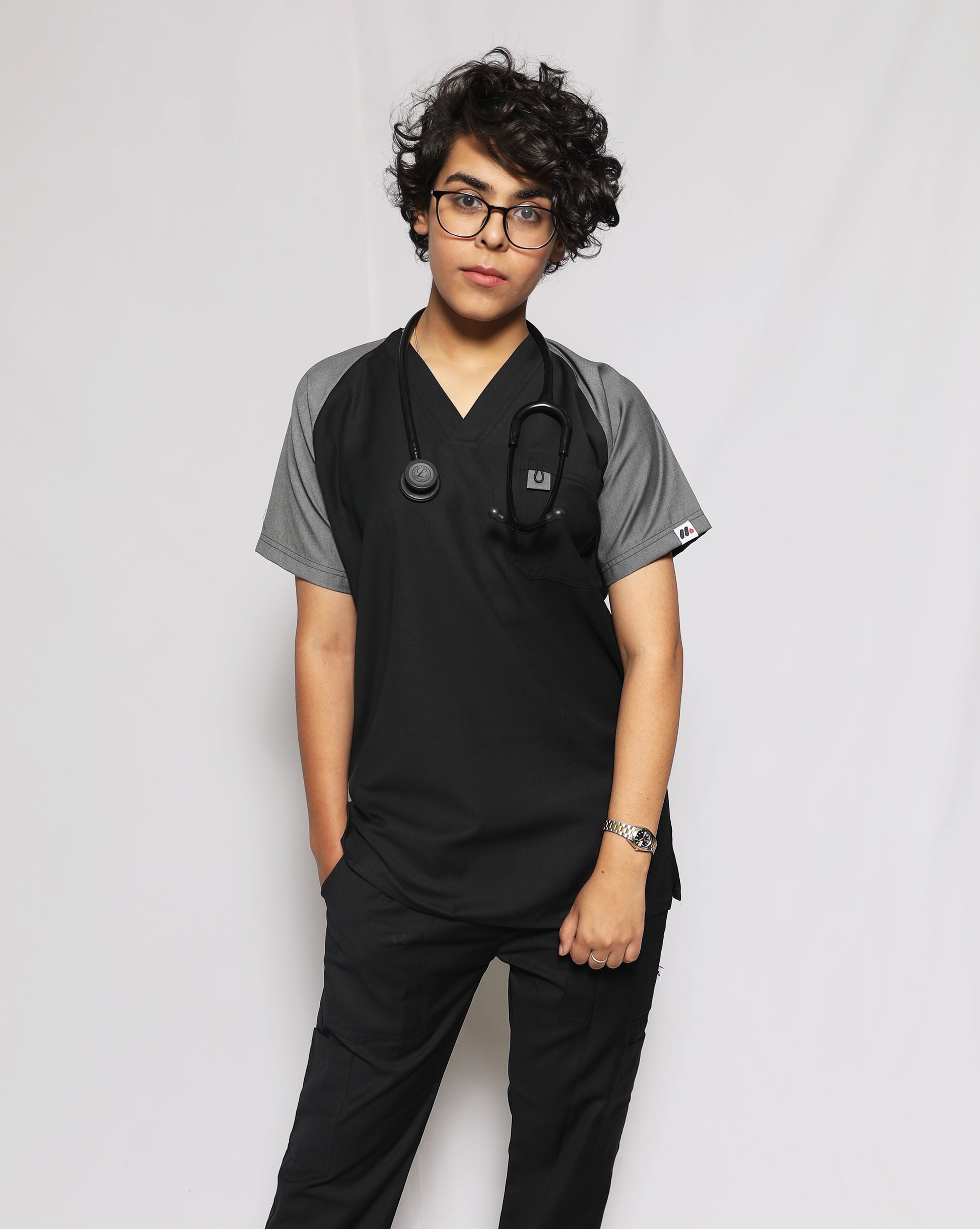Person wearing black medical scrubs with a stethoscope against a plain background.