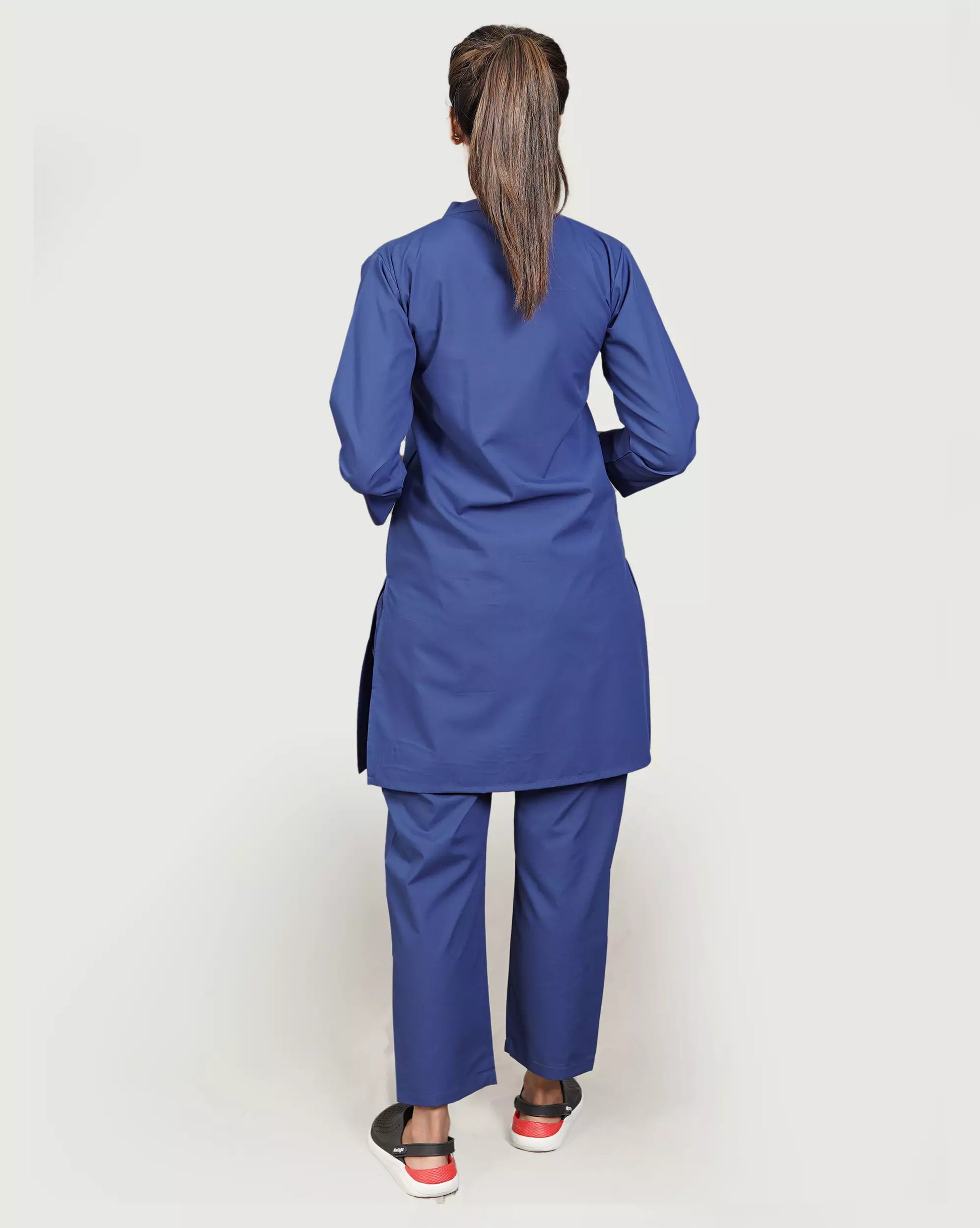 Person wearing a blue lab coat and pants on a plain background