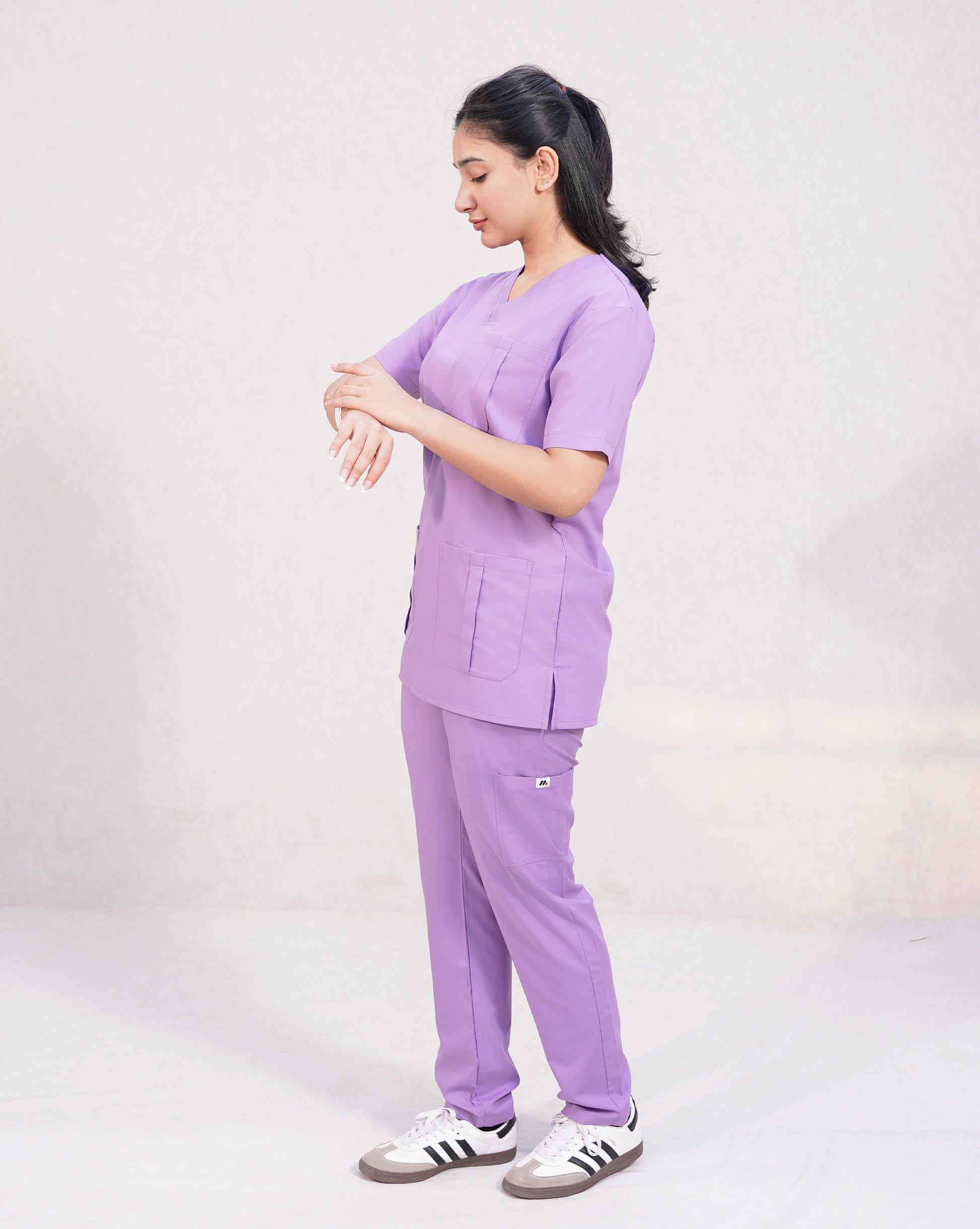 Side profile of a female medical professional in a lavender Medfit Prime Unisex scrub set, adjusting her smartwatch, highlighting comfort and functionality.
