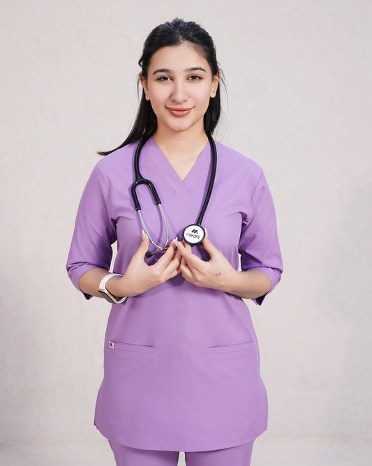 A woman wearing a green scrub set with a V-neckline and 3-quarter sleeves, featuring two bone pockets on the shirt and two pockets on the trousers. She is smiling and standing against a white background.