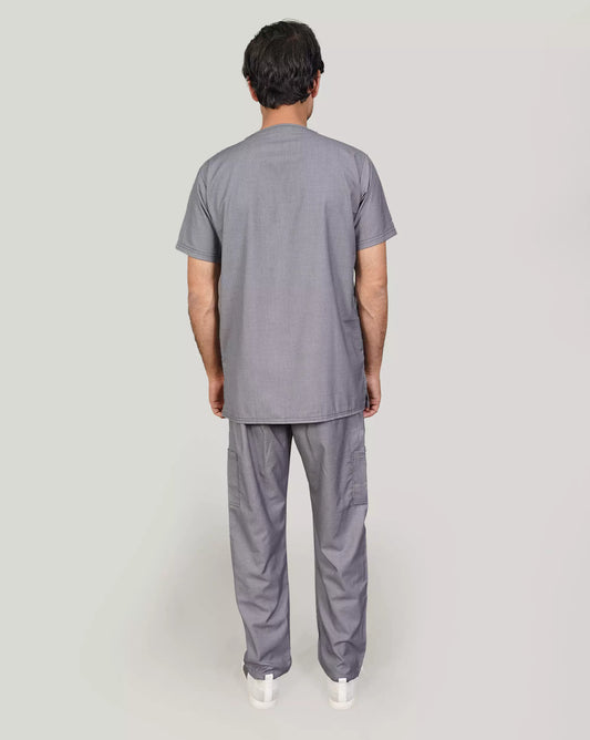 A male doctors wearing a gray V-neckline unisex scrub set with multiple pockets and a name tag, standing against a neutral background.