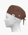 A brown surgical scrub cap with side buttons for face masks worn on a white mannequin head against a neutral gray background.