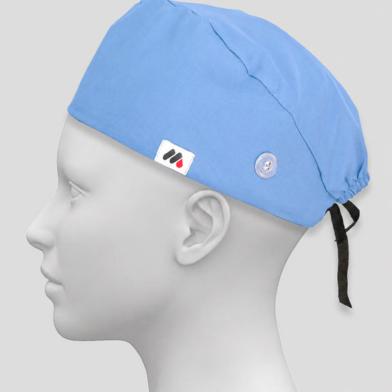 A light blue surgical scrub cap with side buttons for face masks worn on a white mannequin head against a neutral gray background.