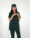 A healthcare professional wearing a dark green medical scrub set, matching scrub cap, and a red-tubed stethoscope around her neck against a white background.