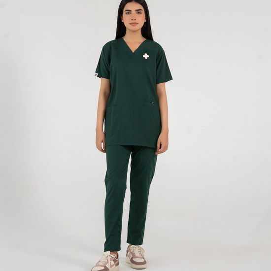 A healthcare professional modeling a dark green V-neck medical scrub set featuring a matching top and pants with a subtle accent pin on the chest against a white background.