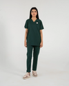A healthcare professional modeling a dark green V-neck medical scrub set featuring a matching top and pants with a subtle accent pin on the chest against a white background.
