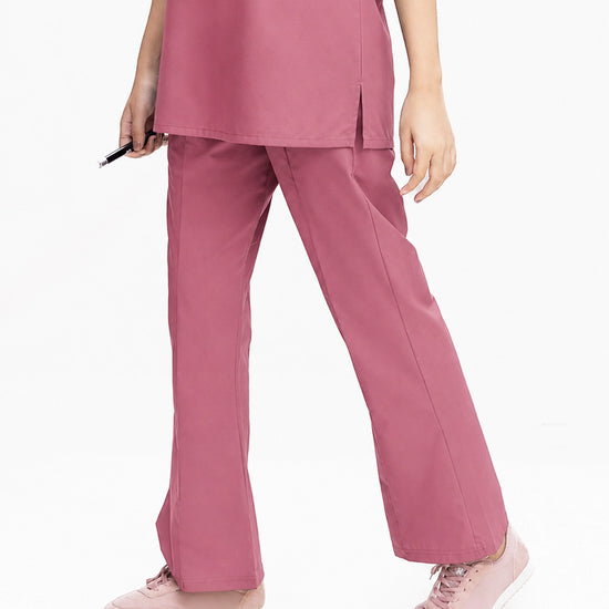 A close-up view of a healthcare professional wearing dusty rose pink medical scrub pants and matching light pink sneakers against a white background.