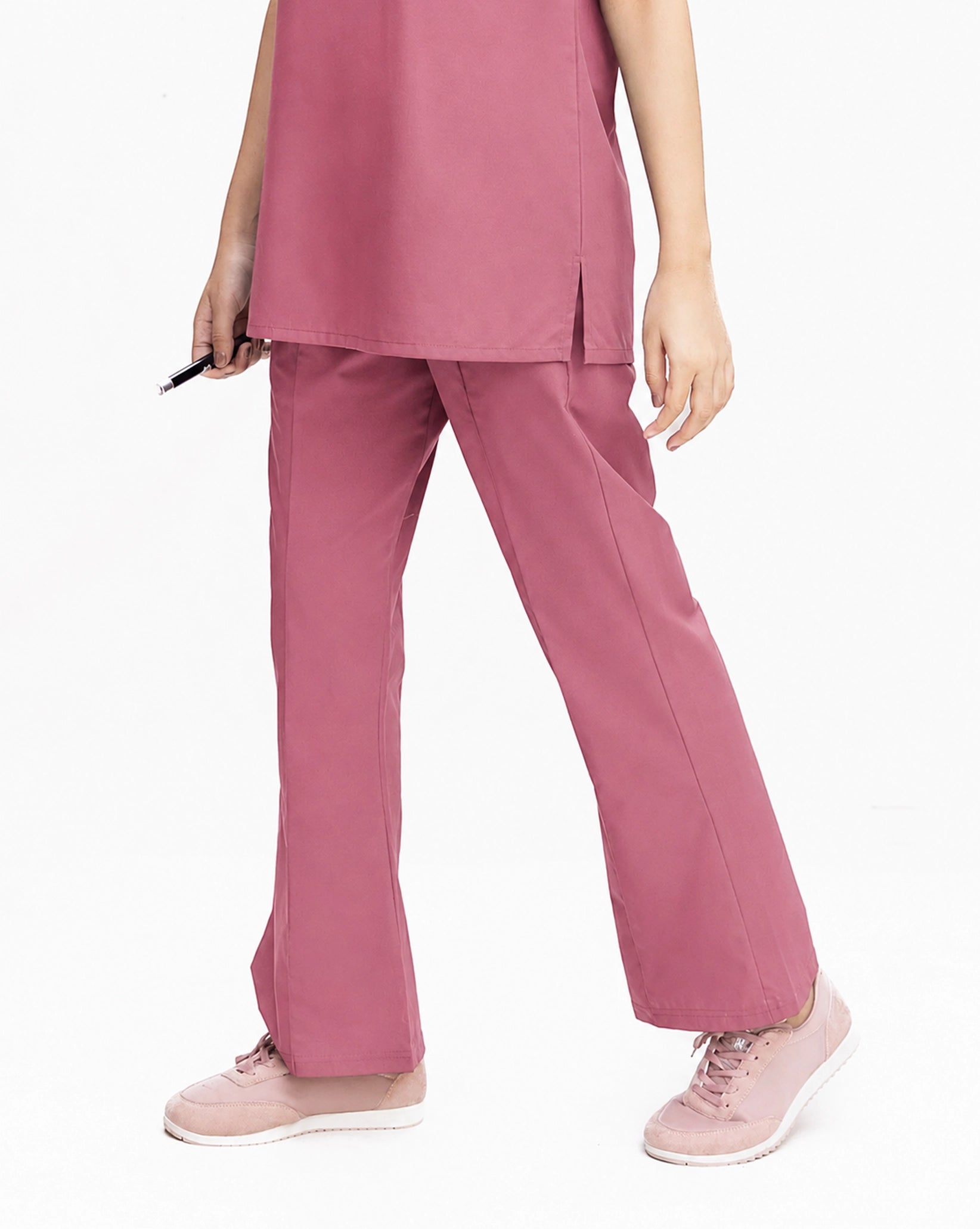 A close-up view of a healthcare professional wearing dusty rose pink medical scrub pants and matching light pink sneakers against a white background.