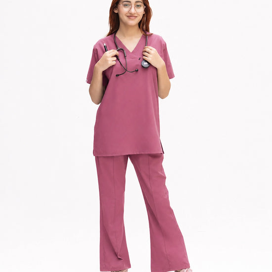 A healthcare professional modeling a matching two-piece medical scrub set in dusty rose pink, featuring a short-sleeve V-neck top and straight-leg pants against a white background.