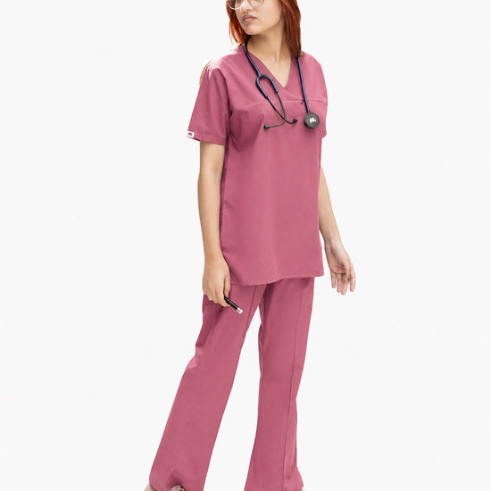 A healthcare professional modeling a matching dusty rose pink medical scrub set from a side angle, wearing a V-neck top and straight-leg pants with a stethoscope.