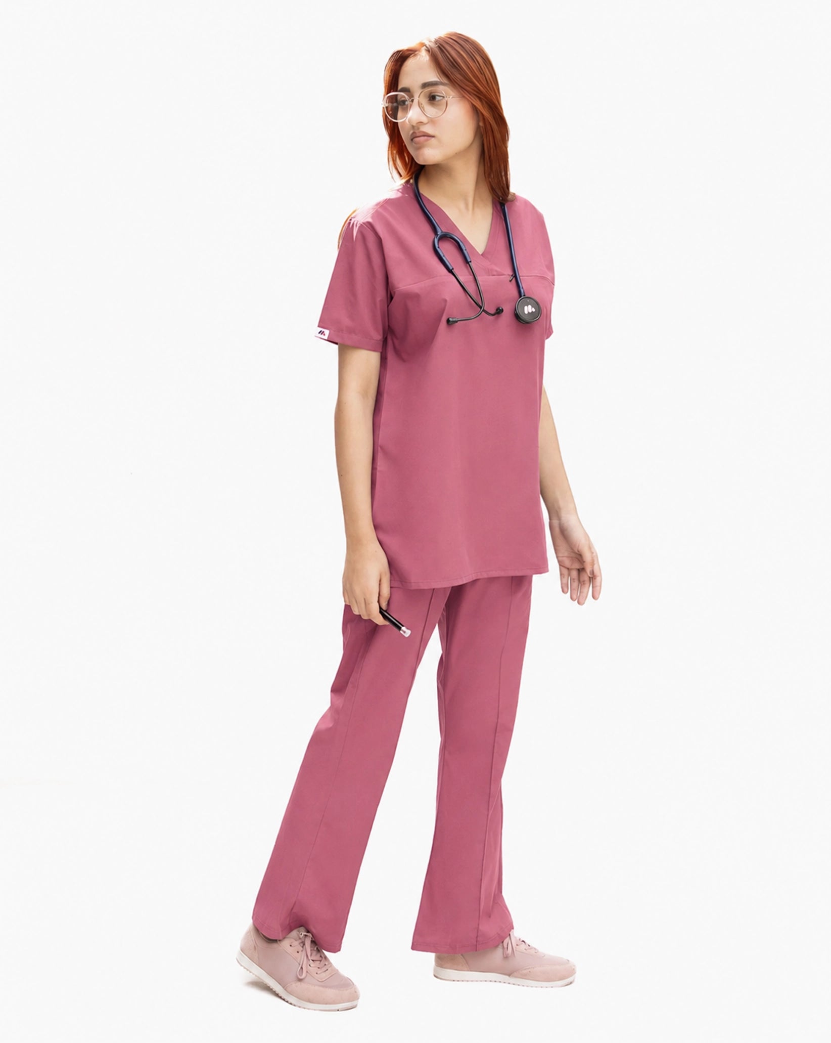 A healthcare professional modeling a matching dusty rose pink medical scrub set from a side angle, wearing a V-neck top and straight-leg pants with a stethoscope.