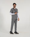 A male healthcare professional standing and modeling a full-body grey medical scrub set over a white long-sleeve undershirt, paired with black sneakers and a stethoscope against a white background.