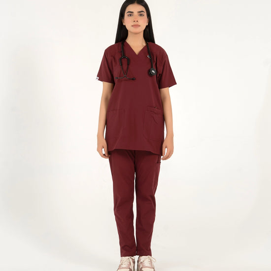 A healthcare professional standing and modeling a full-body maroon medical scrub set with a V-neck top, matching trousers, a stethoscope, and sneakers in a front view pose against a white background.