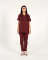 A healthcare professional standing and modeling a full-body maroon medical scrub set with a V-neck top, matching trousers, a stethoscope, and sneakers in a front view pose against a white background.