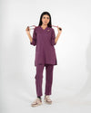 A healthcare professional standing and modeling a full-body purple medical scrub set while holding a stethoscope stretched across her shoulders against a white background.