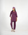 A healthcare professional standing and modeling a full-body purple medical scrub set, matching tooth-pattern scrub cap, stethoscope, and sneakers against a white background.
