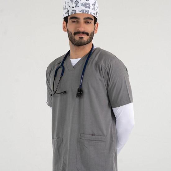 A male healthcare professional wearing a grey V-neck medical scrub top over a white long-sleeve shirt, paired with a patterned medical scrub cap and a stethoscope against a white background.