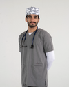 A male healthcare professional wearing a grey V-neck medical scrub top over a white long-sleeve shirt, paired with a patterned medical scrub cap and a stethoscope against a white background.