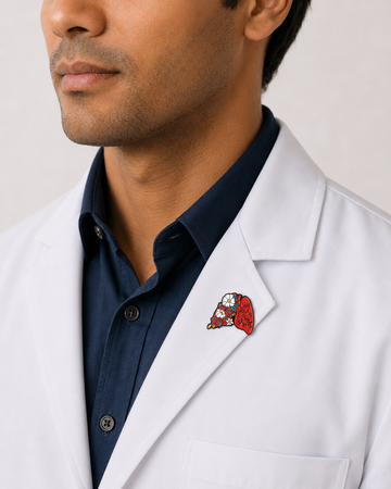 A close-up of a male healthcare professional wearing a white lab coat over a dark blue collared shirt with an anatomical lungs enamel lapel pin against a plain background.