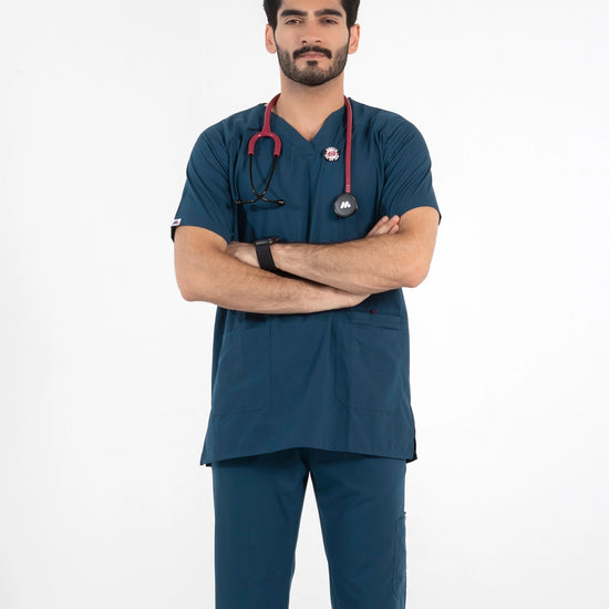 A male model with arms crossed wearing a dark teal-blue V-neck medical scrub top and matching pants, equipped with a red stethoscope, MedFit professional workwear.