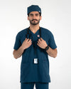 A male model wearing a dark teal blue medical scrub set with a matching surgical cap, stethoscope, and ID badge, MedFit professional medical attire.