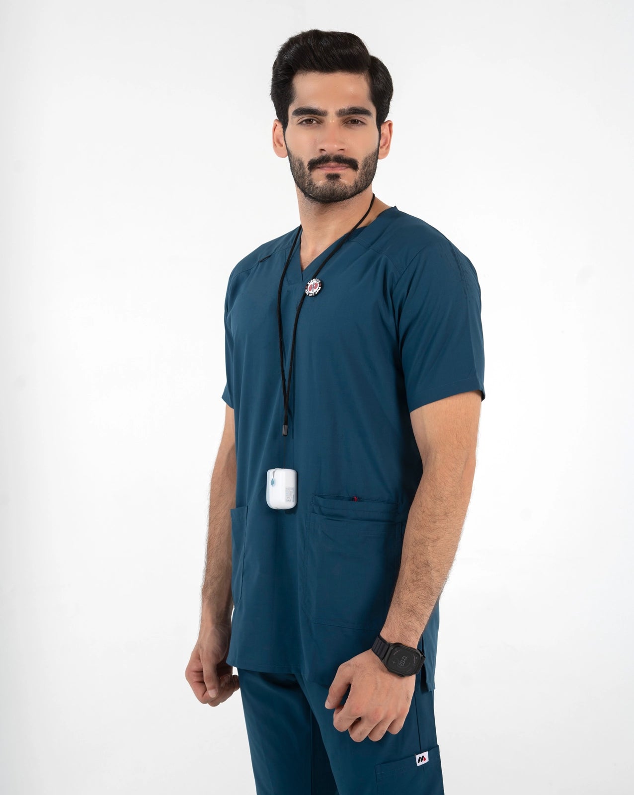 A male model wearing a dark teal blue medical scrub set, featuring a short-sleeve V-neck top with a drawstring and matching scrub pants, MedFit professional healthcare apparel.
