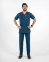 A male model posing in a two-piece dark teal-blue medical scrub set featuring a short-sleeve V-neck top and matching straight-leg pants, wearing a red stethoscope, MedFit.