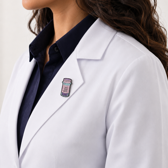A healthcare professional wearing a crisp white lab coat styled with a unique 'Take Your Meds' pill bottle enamel pin on the lapel.