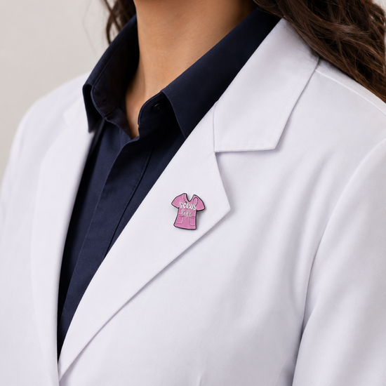 A healthcare professional wearing a white lab coat styled with a cute, pink scrub-top-shaped enamel pin on the lapel.