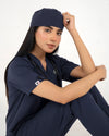 A healthcare professional wearing a matching navy blue medical scrub set with a matching scrub cap and a stethoscope, posing against a white studio background.