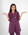A healthcare professional wearing a purple V-neck medical scrub set with a stethoscope and lapel pin, holding her hands open in a welcoming gesture against a white background.