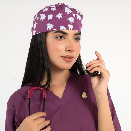 A healthcare professional wearing a purple V-neck medical scrub top, an enamel lapel pin, a matching tooth-pattern scrub cap, and holding a stethoscope against a white background.