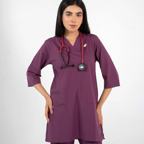 A healthcare professional wearing a purple V-neck medical scrub top with a lapel pin and a stethoscope around her neck against a white background.